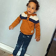 Aïdenn participe au concours pour gagner de l'argent avec cette photo : toddler, child, barefoot, curly_hair, orange_hoodie, denim_jeans, standing, indoor, wooden_floor, wall, casual, pose, looking_away, young_child, curious, clothing, person, portrait, flooring, home