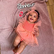 élyne a rejoint le concours — aidez-le/la à gagner de superbes lots ! baby, blanket, card, child, coral, cute, dress, floor, happy, headband, indoors, infant, lying_down, number, person, pink, portrait, smiling, tulle, wooden_floor