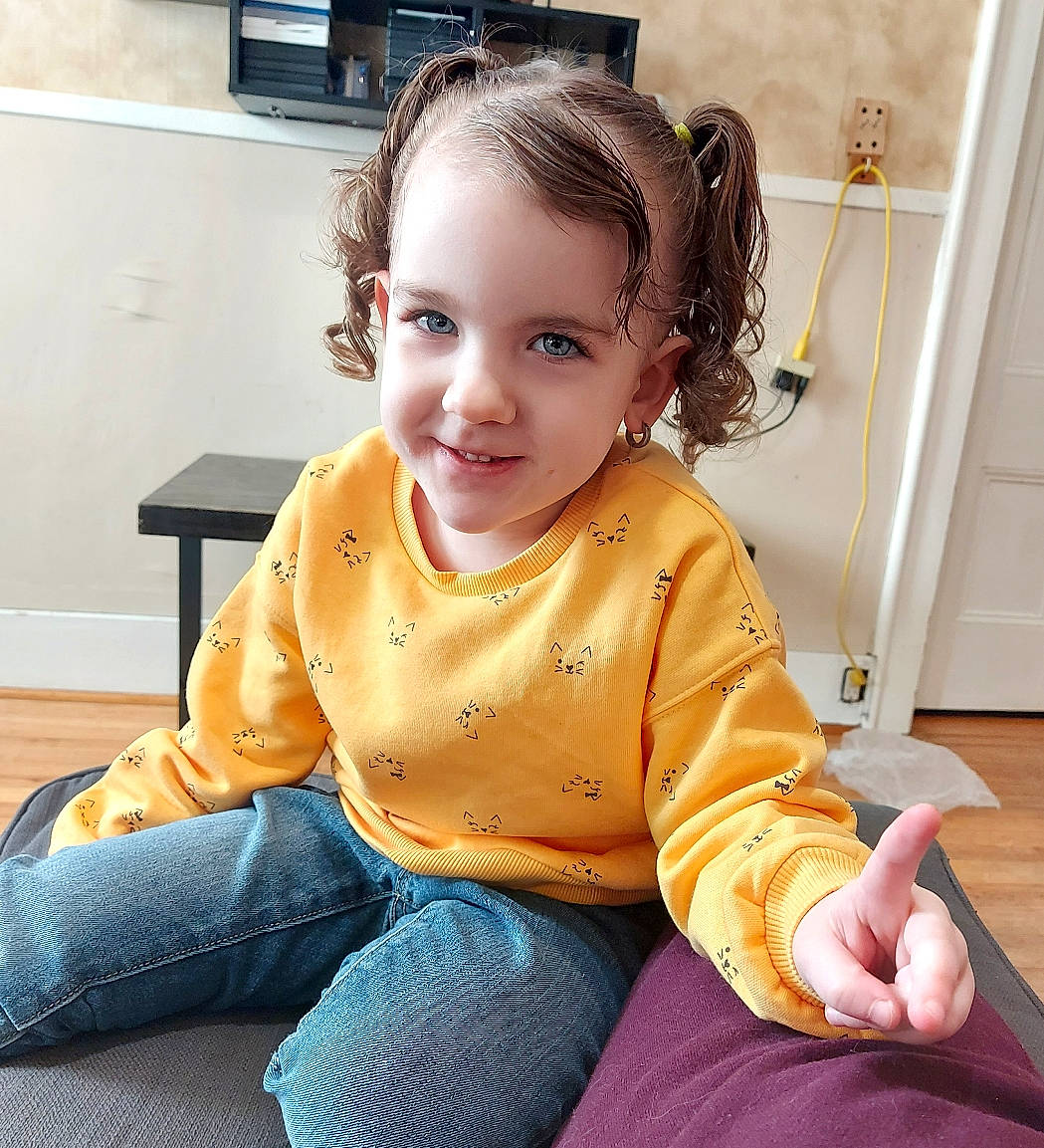 Jayme is registered to the contest to win money with this photo: audio_equipment, baby_toddler_clothing, cheek, child, comfort, ear, floor, flooring, happy, hardwood, hearing, jeans, joy, neck, person, sitting, skin, sleeve, smile, television