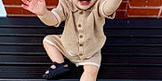 Jack is registered to the contest to win money with this photo: toddler, child, smiling, happy, sitting, bench, brick_wall, sandals, beige_clothing, blue_eyes, outdoor, portrait, cute, hands_up, young_child, knitwear, joyful, person, casual, daylight