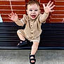 toddler, child, smiling, happy, sitting, bench, brick_wall, sandals, beige_clothing, blue_eyes, outdoor, portrait, cute, hands_up, young_child, knitwear, joyful, person, casual, daylight