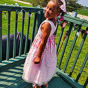Ryann is registered to the contest to win money with this photo: child, girl, pink_dress, smile, outdoor, deck, string_lights, greenery, sunny, flowers, shoes, braided_hair, ribbon, earrings, nature, fence, happy, portrait, summer, holiday