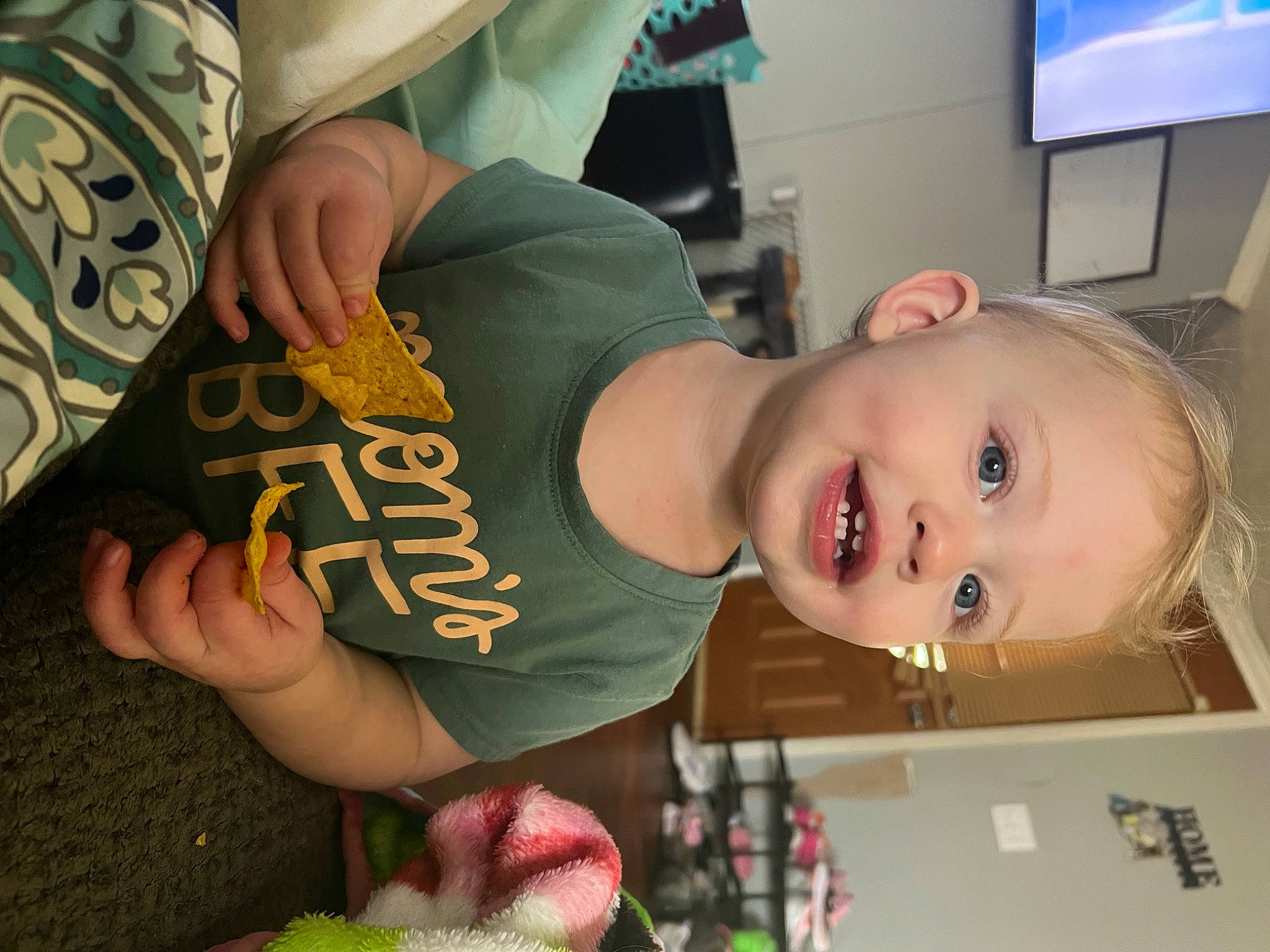 Ella is registered to the contest to win money with this photo: baby, chair, chest, child, elbow, eyelash, finger, food, fruit, fun, happy, hat, home_appliance, mouth, person, plant, room, smile, t_shirt, television