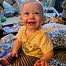 baby, child, smiling, happy, laughing, portrait, sitting, indoor, toys, stuffed_penguin, playroom, yellow_shirt, striped_pants, blanket, cushion, baby_bottle, infant, face, home, colorful