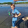 Yoni a rejoint le concours — aidez-le/la à gagner de superbes lots ! boy, child, water, splash, blue_shirt, denim_shorts, barefoot, fanta_can, shoes, outdoor, sunny_day, river, playing, water_bottle, tattoo, shadow, pavement, trees, sky, fun