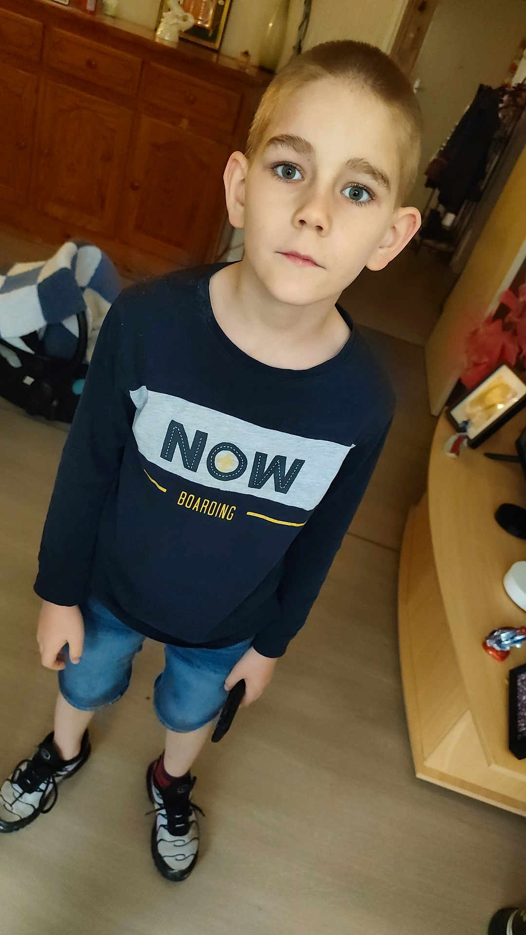 Yoni participe au concours pour gagner de l'argent avec cette photo : boy, child, indoor, portrait, casual_clothing, shorts, sneakers, phone, buzz_cut, blue_eyes, standing, looking_at_camera, home_interior, cabinet, floor, curiosity, young, person, furniture, shirt