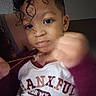 Za'Khi is registered to the contest to win money with this photo: child, toddler, curly_hair, face, expression, hand, fist, necklace, clothing, shirt, text_on_shirt, indoor, person, portrait, young_child, casual, closeup, skin, earring, looking_at_camera