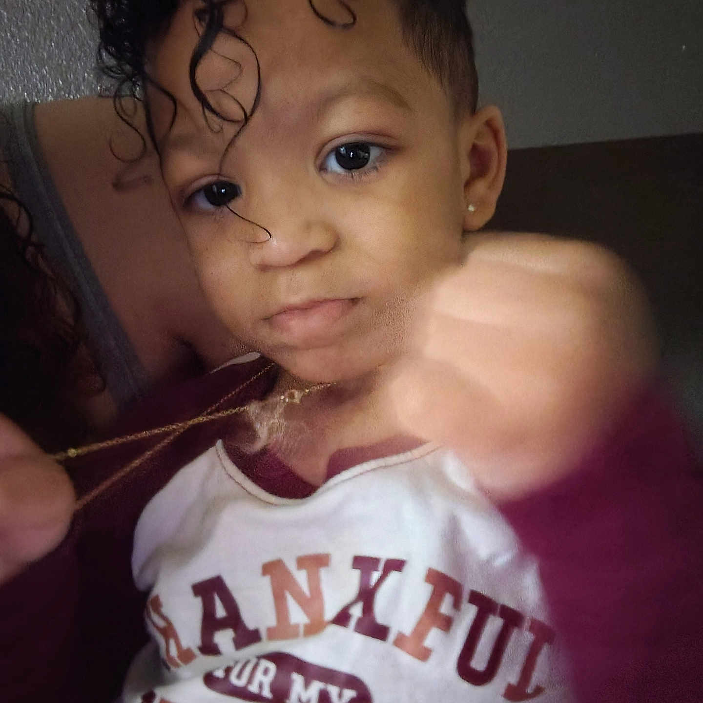 Za'Khi is registered to the contest to win money with this photo: child, toddler, curly_hair, face, expression, hand, fist, necklace, clothing, shirt, text_on_shirt, indoor, person, portrait, young_child, casual, closeup, skin, earring, looking_at_camera