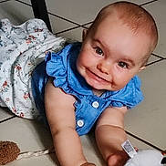 Maëly a rejoint le concours — aidez-le/la à gagner de superbes lots ! baby, child, smiling, blue_dress, toy, floor, tile, blanket, indoor, person, cute, infant, happy, face, arm, hand, play, clothing, furniture, home