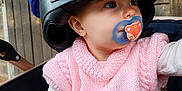 Maëly a rejoint le concours — aidez-le/la à gagner de superbes lots ! baby, helmet, pacifier, pink_vest, knitted_clothing, shark_design, hand, stroller, wooden_background, child, cute, infant, clothing, sitting, portrait, face, eyes, indoor, person, pacifier_clip