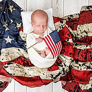 Michael is registered to the contest to win money with this photo: baby, newborn, sleeping, blanket, flag, american_flag, wooden_floor, pillow, wrapped, patriotic, infant, peaceful, caucasian_baby, small_flag, red, white, blue, stars, stripes, floor
