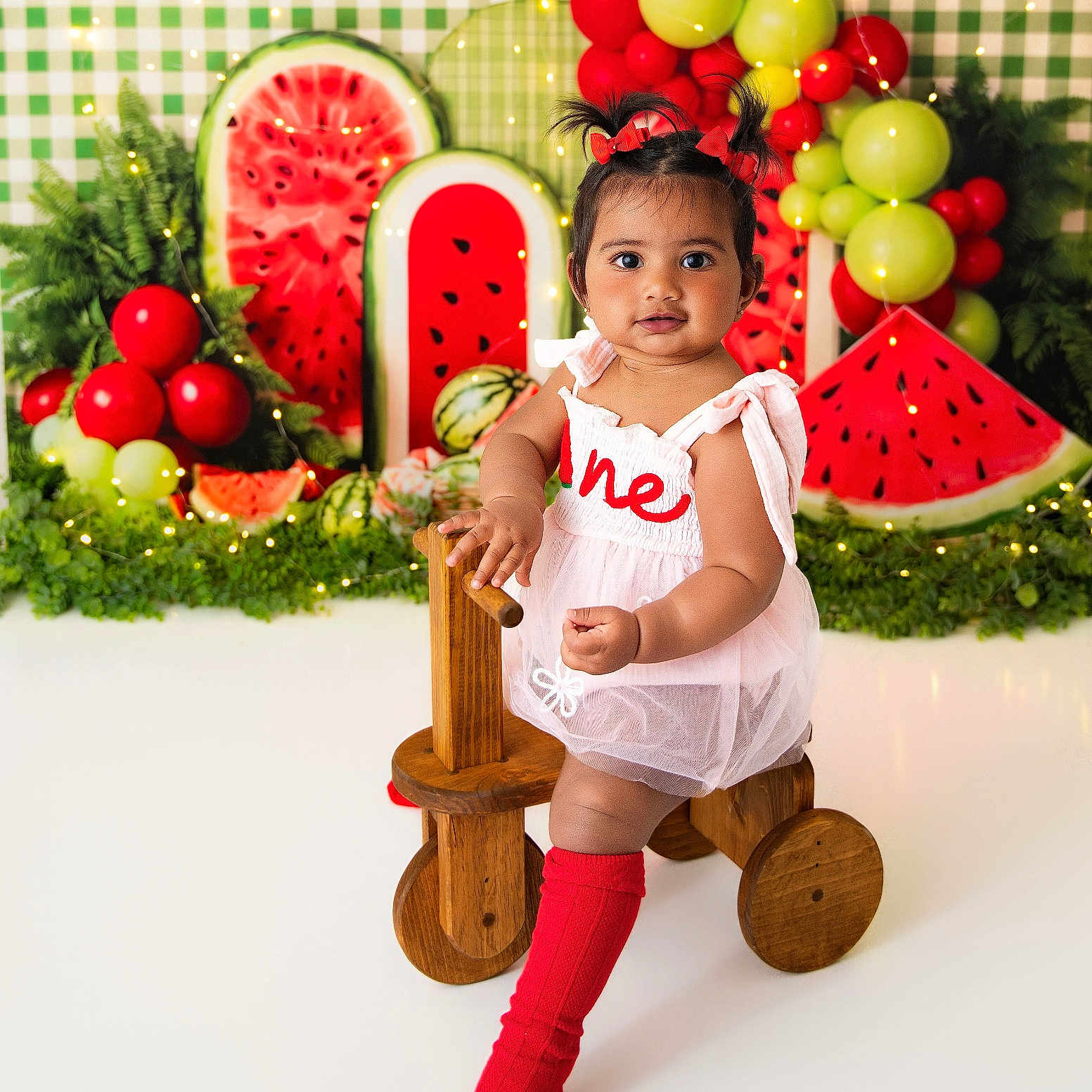 Aarna is registered to the contest to win money with this photo: baby, child, toddler, wooden_toy, toy_bike, red_socks, pink_dress, balloons, watermelon_decor, greenery, party, celebration, indoor, portrait, smiling, cute, festive, colorful, happy, young_child