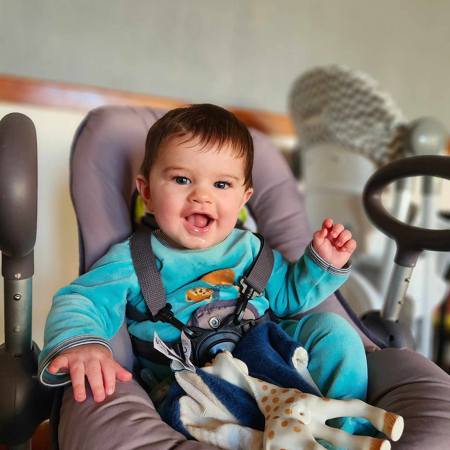 Hélio a rejoint le concours — aidez-le/la à gagner de superbes lots ! baby, baby_seat, blanket, blue_clothing, bokeh_background, child, drooling, eyes, face, feeding_chair, hair, hand, happy, harness, highchair, indoor, infant, playful, smiling, toy_giraffe