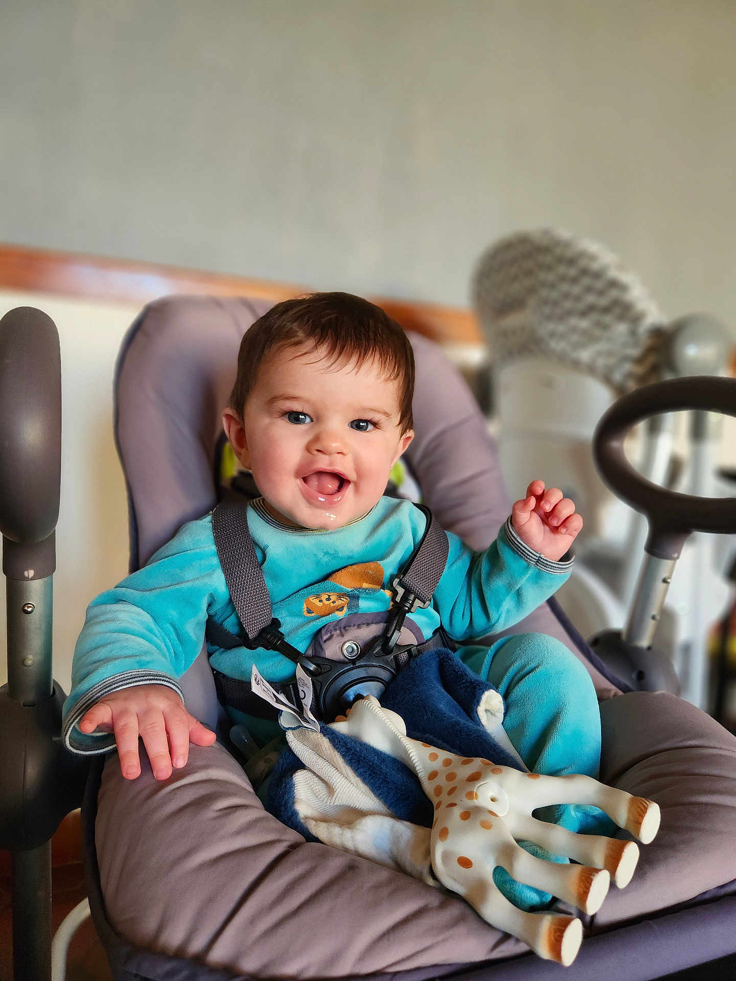 Hélio a rejoint le concours — aidez-le/la à gagner de superbes lots ! baby, infant, child, smiling, drooling, blue_clothing, baby_seat, highchair, harness, toy_giraffe, blanket, hand, face, eyes, happy, hair, indoor, bokeh_background, feeding_chair, playful