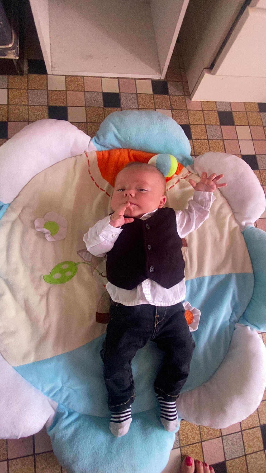 Lorenzo participe au concours pour gagner de l'argent avec cette photo : baby, child, infant, vest, striped_socks, cushioned_mat, floor_tiles, hand, feet, toenails, clothing, indoor, person, laying_down, curious_expression, colorful, soft_toy, fabric, floor, footwear
