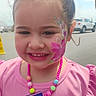 child, girl, face_paint, pink_bow, pink_shirt, necklace, snack, chips, outdoor, daylight, smile, portrait, vehicle, road, hand, accessory, happy, colorful, young_child, casual