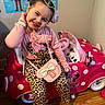 child, girl, smiling, pink_clothing, leopard_print, toy_car, minnie_mouse, indoor, wooden_floor, hair_accessory, purse, playful, pose, education_poster, floor, boots, happy, cute, accessories, room