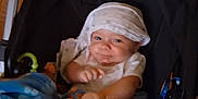 Johnny is registered to the contest to win money with this photo: baby, blanket, blue, orange, paws, stroller, child, infant, smile, cloth, headwear, indoor, floor, wooden_floor, seat, toy, playful, cute, person, cozy