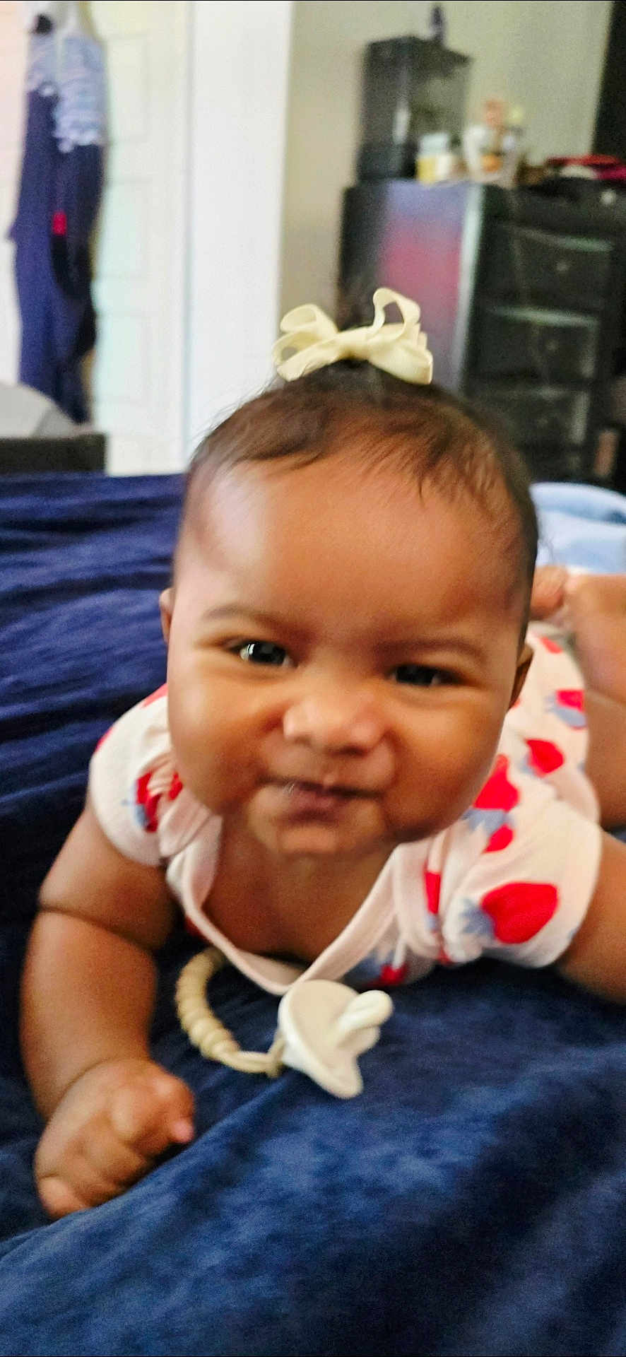 Ahnya-Ann joined the competition — help win amazing prizes! baby, infant, pacifier, bow, blue_blanket, white_clothing, red_pattern, lying_down, face, portrait, cute, child, indoors, furniture, background, smile, hand, head, skin, expression