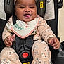 baby, child, smiling, car_seat, headband, floral_clothing, socks, infant, happy, cute, indoors, seatbelt, black_car_seat, pink, clothing, portrait, baby_accessory, baby_bib, baby_toy, baby_safety