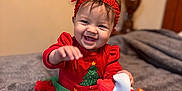 Aurora joined the competition — help win amazing prizes! baby, child, smiling, red_headband, christmas_outfit, toy, gingerbread_man, plush_toy, indoor, bed, blanket, holiday, festive, cute, toddler, happy, person, sitting, striped_leggings, christmas_tree_design