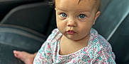 Aurora is registered to the contest to win money with this photo: baby, child, blue_eyes, curly_hair, floral_clothing, car_seat, infant, portrait, cute, sitting, indoor, person, young_child, skin, hand, foot, clothing, looking, expression, cute_face