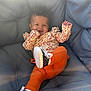 baby, child, smiling, curly_hair, orange_pants, sneakers, couch, cushion, indoor, happy, playful, infant, clothing, portrait, person, cute, relaxing, toddler, seat, cozy