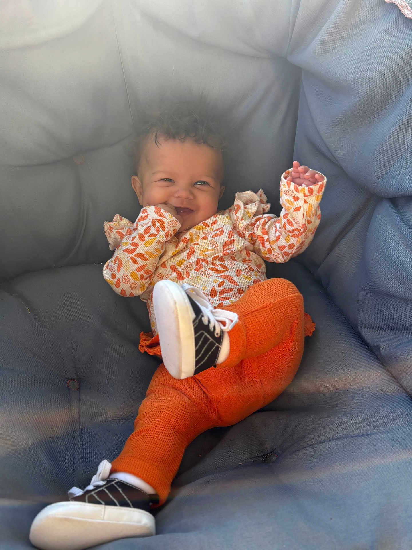Aurora is registered to the contest to win money with this photo: baby, child, smiling, curly_hair, orange_pants, sneakers, couch, cushion, indoor, happy, playful, infant, clothing, portrait, person, cute, relaxing, toddler, seat, cozy