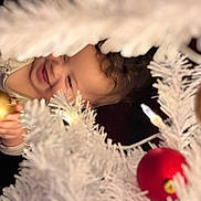 Aurora is registered to the contest to win money with this photo: child, toddler, smiling, face, christmas_tree, white_tree, ornament, red_ornament, gold_ornament, holiday, festive, celebration, decorations, happy, curly_hair, indoor, holiday_lights, joyful, seasonal, holding