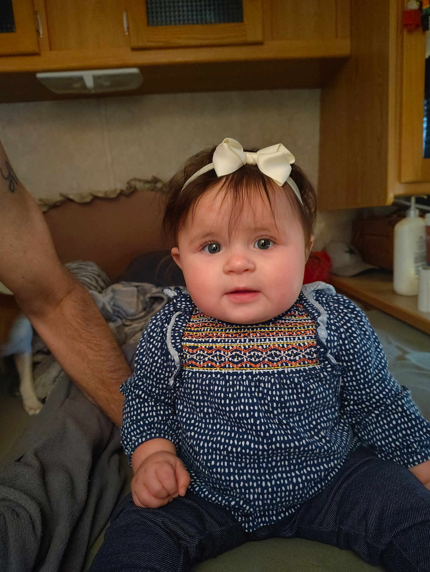 Daeneris is registered to the contest to win money with this photo: arm, baby, blanket, blue_clothing, bow, child, cozy, cute, eyes, face, furniture, hair, hand, headband, indoor, infant, patterned_clothing, person, sitting, tattoo