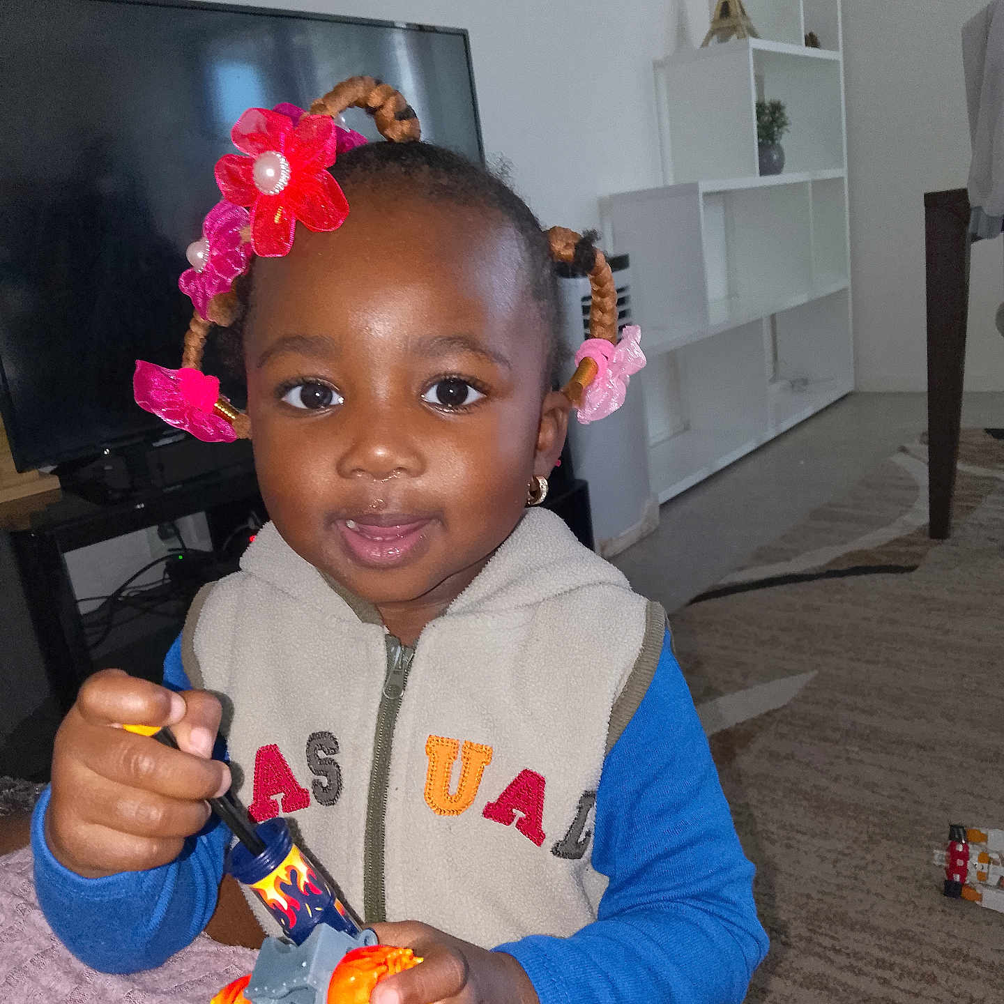 Assial a rejoint le concours — aidez-le/la à gagner de superbes lots ! car_toy, carpet, child, clothing, earrings, face, furniture, hair_accessories, hand, indoor, person, portrait, room, shelf, smiling, sweater, table, television, toddler, toy