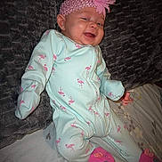 Londyn is registered to the contest to win money with this photo: baby, infant, onesie, pink_flower, headband, flamingo_pattern, pink_booties, pacifier, cushion, bedspread, smiling, cheerful, clothing, indoor, child, cute, resting, portrait, person, baby_girl