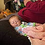 baby, sleeping, blanket, crochet, cushion, person, adult, hand, maroon_clothing, indoor, cozy, relaxing, home, soft_focus, resting, infant, comfort, pink, blue, green