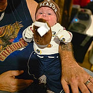 Zaylen joined the competition — help win amazing prizes! adult, arms, baby, child, clothing, face, family, football, hat, indoor, infant, onesie, pants, plush_toy, portrait, sitting, smiling, socks, sports_fan, toy