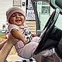 baby, car_interior, child, door, face, hand, happy, hat, house, infant, inflatable_decoration, outdoor, person, pink_clothing, plaid_pants, portrait, seat, smiling, steering_wheel, window