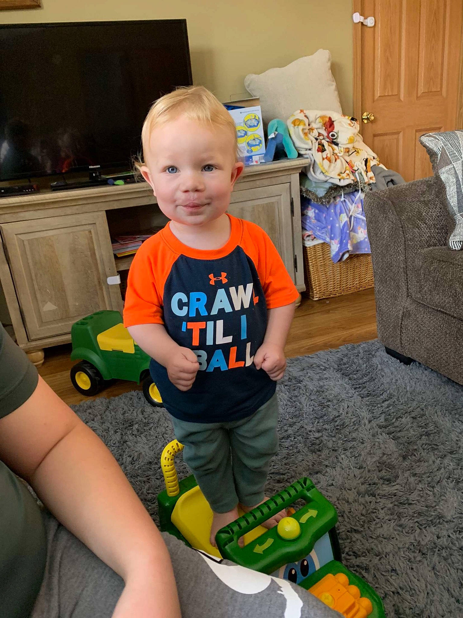 Daxton is registered to the contest to win money with this photo: baby, baby_toddler_clothing, child, floor, flooring, fun, home_appliance, joy, lap, living_room, person, play, product, room, sitting, smile, standing, t_shirt, television, toddler