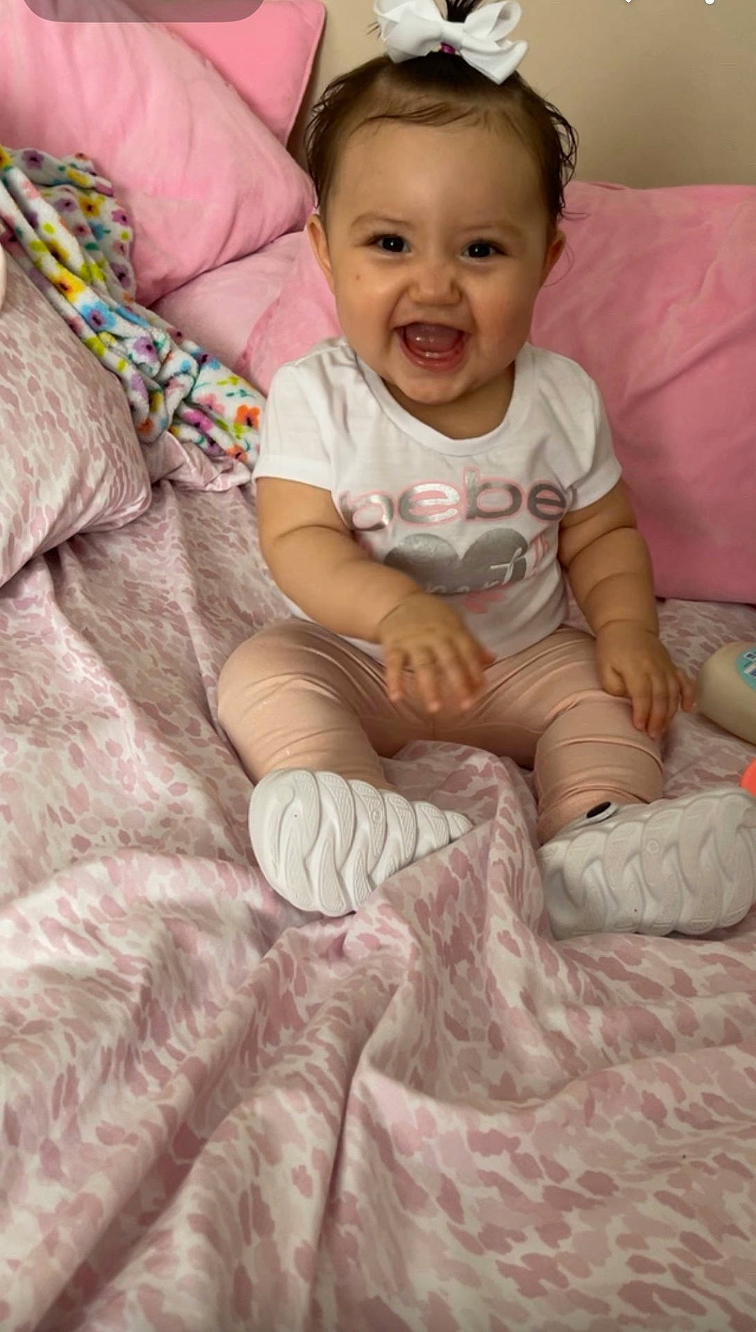 Yareli joined the competition — help win amazing prizes! baby, blanket, child, clothing, cute, fashion, happy, home, indoors, infant, joy, person, pillow, pink_bedspread, portrait, sitting, smiling, toddler, white_bow, white_shoes