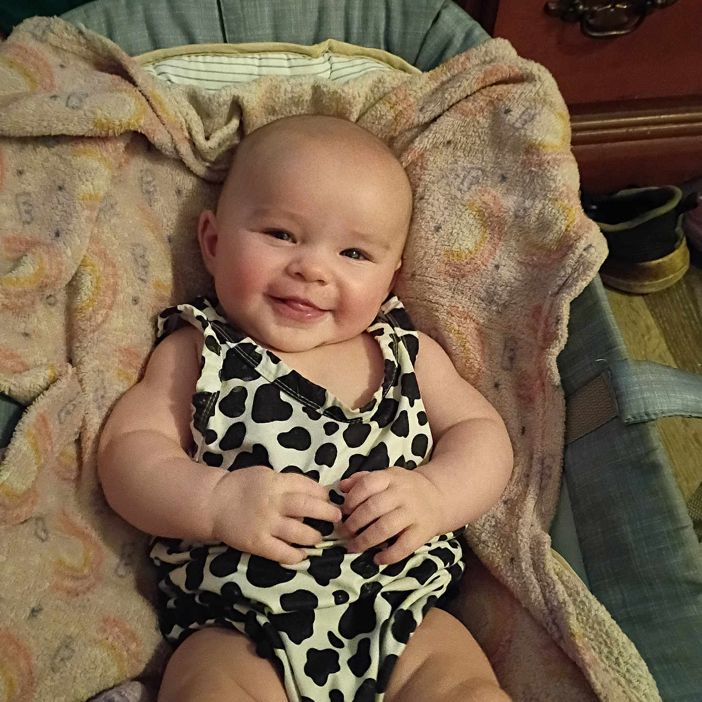October is registered to the contest to win money with this photo: baby, infant, smile, cute, cow_print, blanket, fabric, clothing, person, indoor, furniture, shoe, happy, skin, arm, legs, head, face, home, cozy