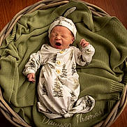Dawson is registered to the contest to win money with this photo: newborn, baby, basket, blanket, wood_floor, sleepwear, hat, yawning, infant, cozy, knit, wood, cute, resting, portrait, sleepy, soft, patterned_clothing, toddler, indoors