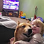 Bindi is registered to the contest to win money with this photo: toddler, dog, hug, indoor, living_room, carpet, toy, television, blanket, laundry_basket, vacuum_cleaner, child, pet, furniture, couch, home, cute, affection, floor, window