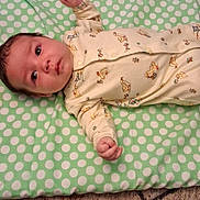 Landon is registered to the contest to win money with this photo: baby, infant, onesie, polka_dot, cushion, carpet, floor, lying_down, child, cute, pattern, animal_print, yellow_clothing, indoor, person, newborn, small_hands, face, eyes_open, soft_surface