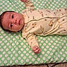 baby, infant, onesie, polka_dot, cushion, carpet, floor, lying_down, child, cute, pattern, animal_print, yellow_clothing, indoor, person, newborn, small_hands, face, eyes_open, soft_surface