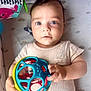 baby, child, toy, ball, curious, blue_eyes, infant, play_area, soft_lighting, cute, hands, clothing, indoors, portrait, looking_at_camera, young, playtime, closeup, expression, colorful
