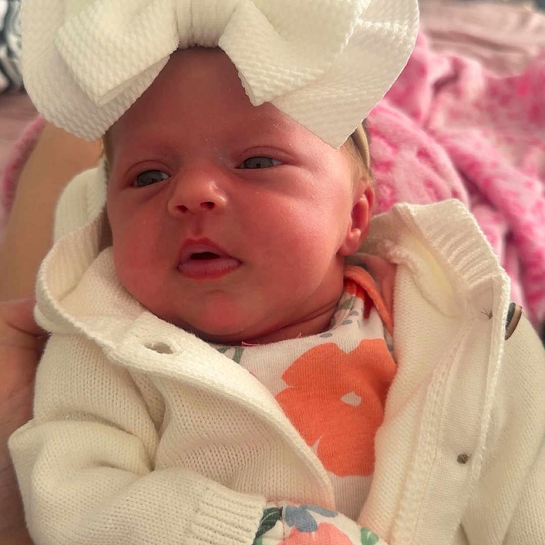 Keygan joined the competition — help win amazing prizes! baby, baby_accessory, baby_girl, closeup, clothing, cozy, cute, face, floral_mittens, hand, indoor, infant, knitted_sweater, newborn, person, pink_blanket, portrait, soft_lighting, warm, white_bow