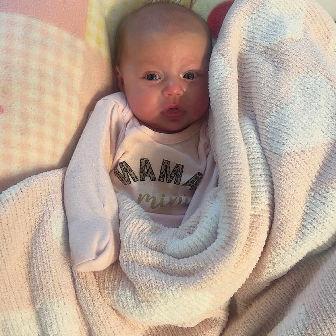 Keygan Alminta is registered to the contest to win money with this photo: baby, blanket, child, clothing, cozy, cute, expression, face, floor_tiles, indoor, infant, looking, newborn, person, pink, portrait, soft_texture, swaddled, warm, white