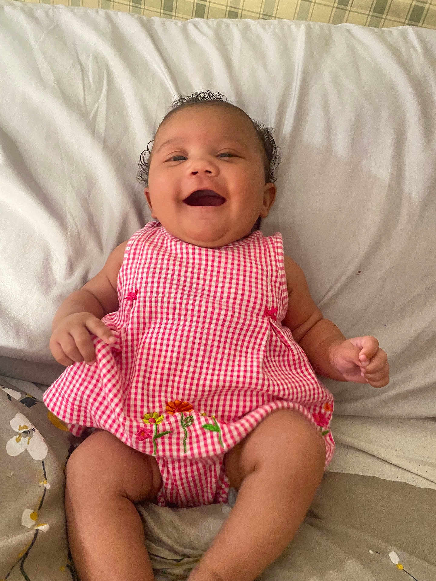 Jordan joined the competition — help win amazing prizes! baby, infant, smiling, happy, lying_down, bed, pillow, blanket, gingham_pattern, pink_dress, floral_embroidery, chubby_cheeks, curly_hair, cute, portrait, indoor, skin, hands, legs, nursery