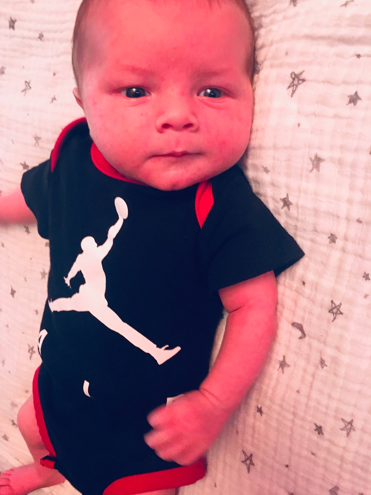 Maddux is registered to the contest to win money with this photo: arm, baby, cheek, child, cool, eye, face, head, lip, nose, outerwear, person, pink, play, red, skin, sleeve, smile, standing, t_shirt