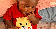 Eliyanah joined the competition — help win amazing prizes! baby, child, infant, portrait, smiling, sitting, bed, blanket, pillow, red_shirt, bear_design, strawberry_pattern, pink_clothing, finger_nibbling, indoor, bedroom, cozy, cute, dark_skin, playful