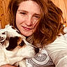 woman, dog, cuddle, smile, red_hair, white_sweater, indoor, wooden_wall, pet, closeup, portrait, face, animal, friendship, cozy, casual, love, hand, ring, resting