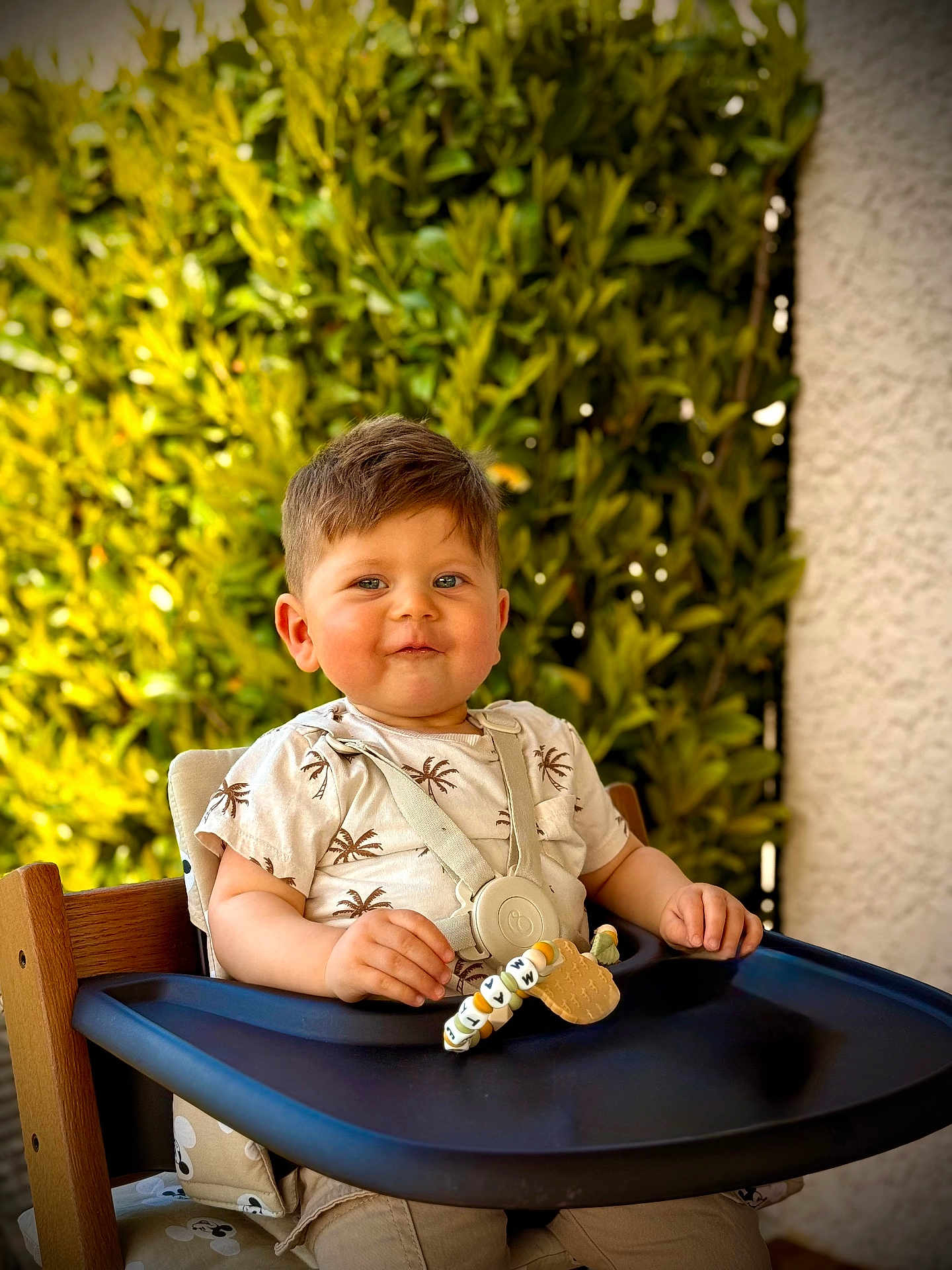 Mateo a rejoint le concours — aidez-le/la à gagner de superbes lots ! toddler, child, high_chair, smile, baby, outdoor, greenery, leafy_background, sunlight, clothing, seatbelt, wooden_chair, face, happy, cute, portrait, summer, casual_wear, baby_toy, playful